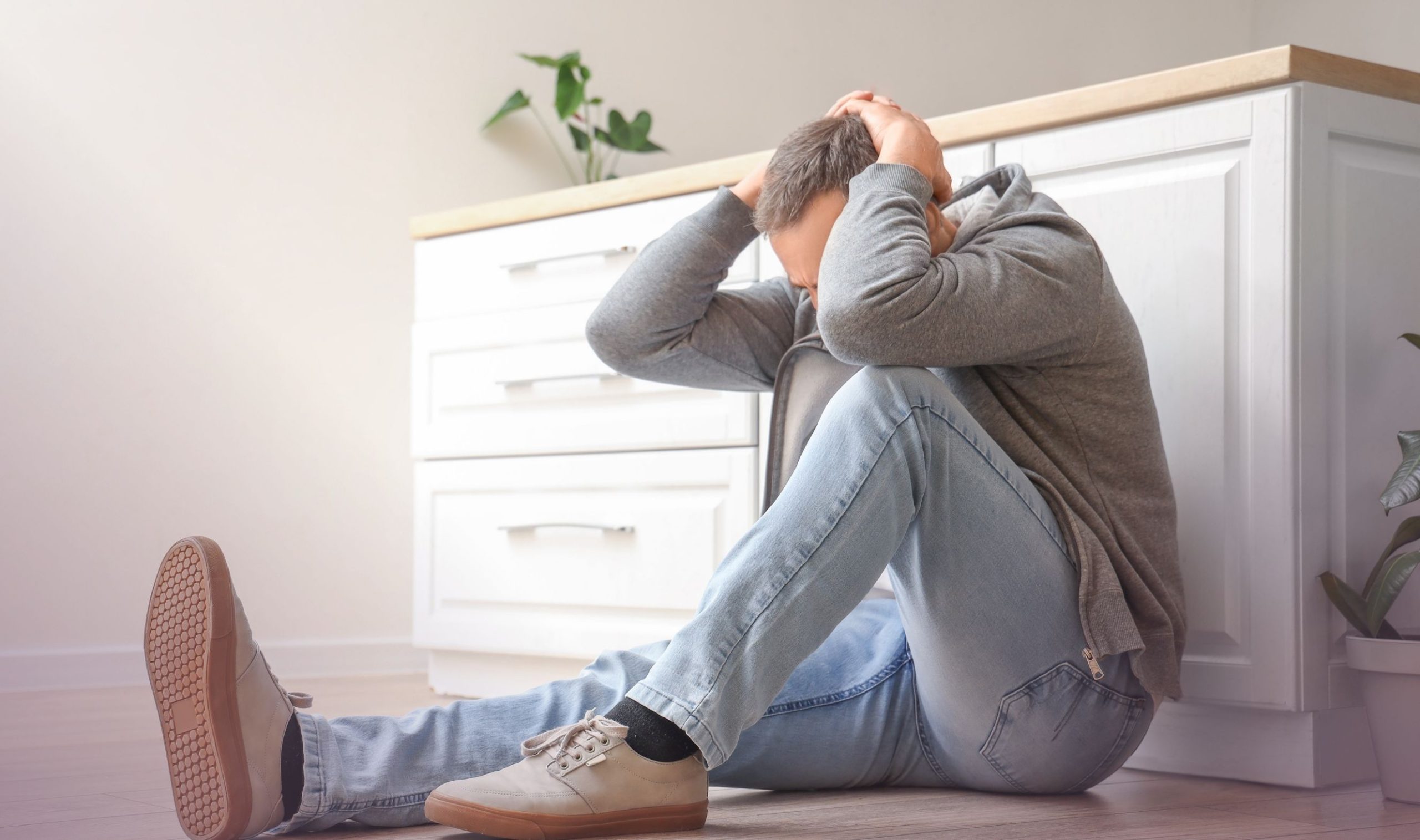 Ein Mann mit Angst und Panikstörung versteckt sich hinter einer Kommode, die Hände über dem Kopf verschränkt